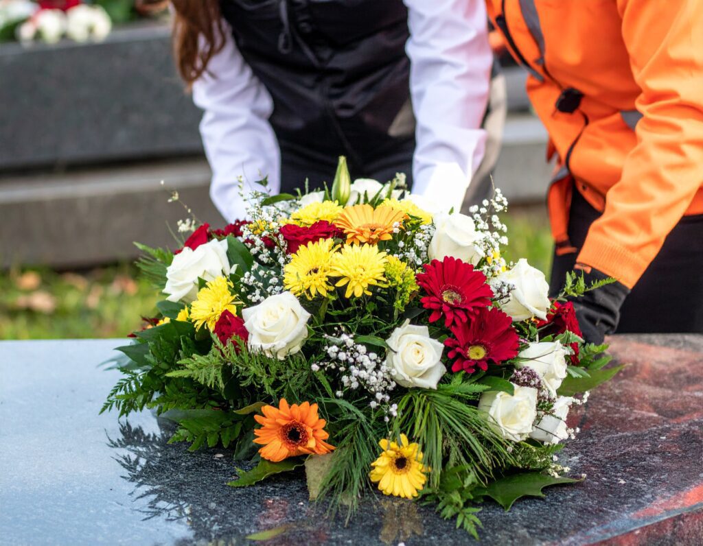 Pracownik firmy Lorem dostarcza wiązankę kwiatów na cmentarz w Olsztynie.